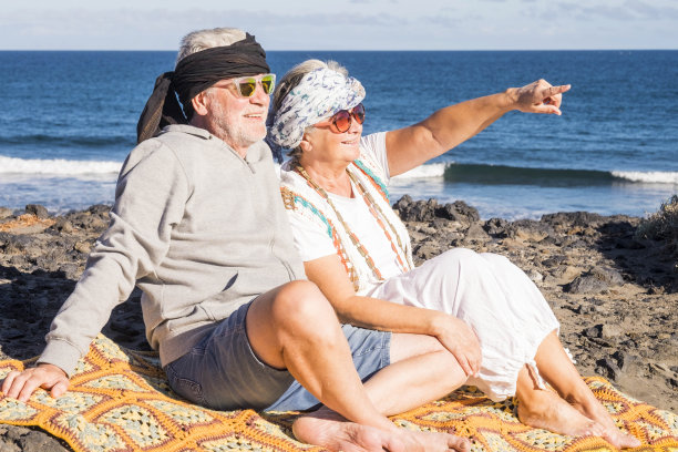 一对快乐的老年白种人坐在海滩上享受夏天的时间和太阳。嬉皮士的另类服装真正的自由和幸福在一起图片下载
