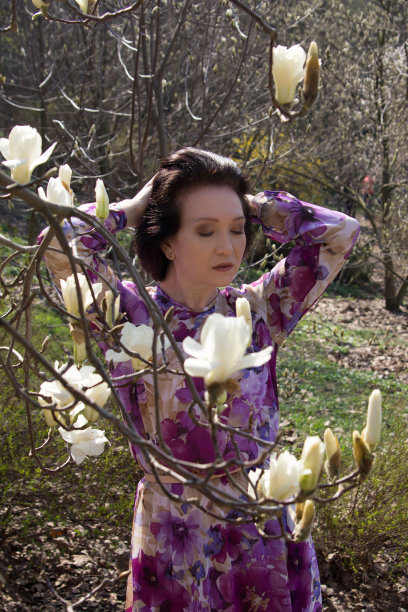 户外一个年轻美丽的女子肖像附近的木兰树与花。女孩穿着优雅的裙子。图片下载