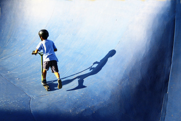 穿着蓝色t恤的男孩在滑板公园的蓝色斜坡上骑着滑板车图片下载