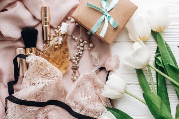 时尚的工艺礼品盒、蕾丝内衣、珠宝和香水，置于柔软的织物上，白色背景上点缀着郁金香。节日女性必备品俯视图。Instagram照片图片下载
