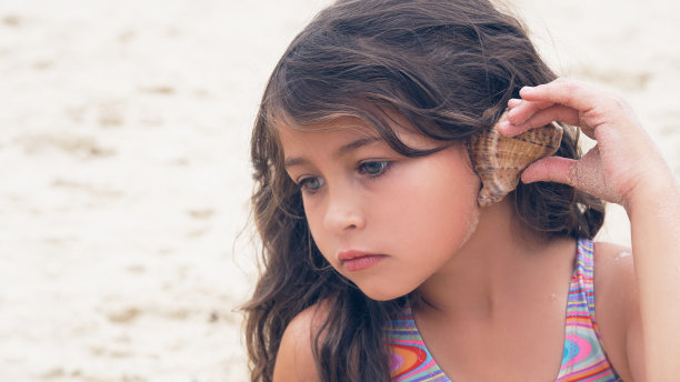 美丽的小女孩，长卷发，在海滩上听着海歌图片下载