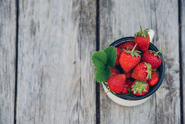 新鲜多汁的带叶草莓。质朴的搪瓷马克杯和手工花边。复古的杂志图片。图片下载