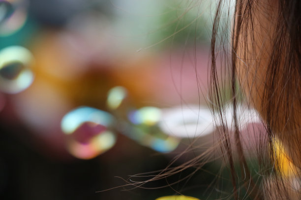 旁边的女孩头发，她吹着泡沫和玩着泡沫在公园里五颜六色的自然模糊的背景图片下载