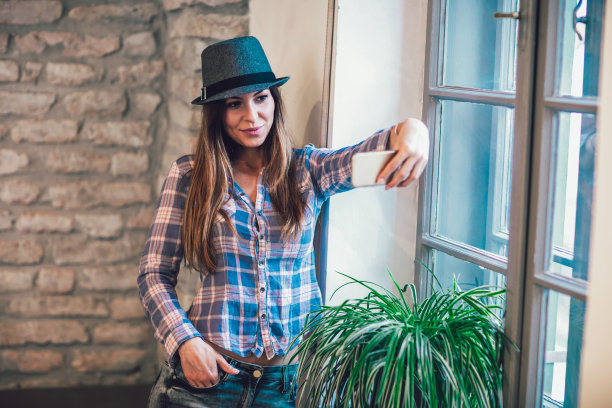 年轻微笑的女性用智能手机自拍。图片下载