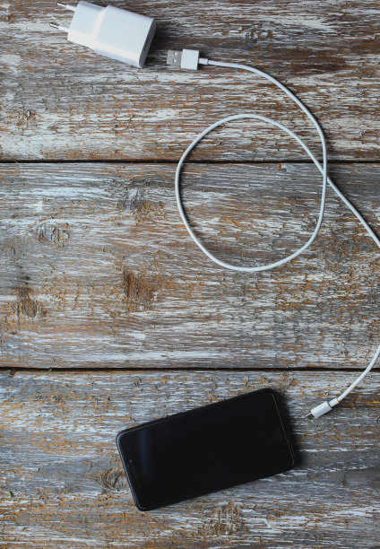 白色充电器和黑色智能手机在旧的木制背景。信息技术垂直数码照片。复古纹理上的现代布局。图片下载