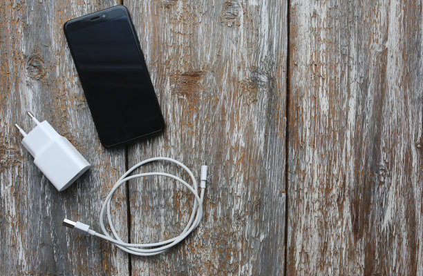 白色充电器和黑色智能手机在旧的木制背景。信息技术水平数码照片。复古纹理上的现代布局。图片下载