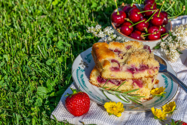 两份樱桃蛋糕的横向照片。蛋糕放在托盘上，用白毛巾垫着。碗里装满了其他水果，旁边是点缀着几颗红草莓和花朵的蛋糕。图片下载