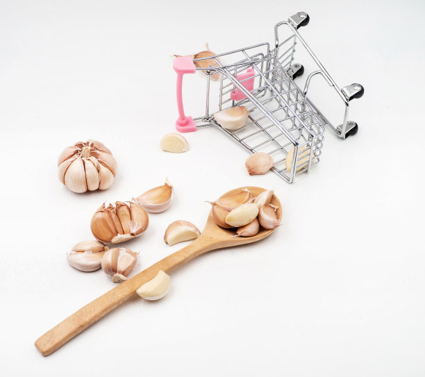 放着大蒜的木勺，旁边放着大蒜头和掉落的购物车，背景白色图片下载