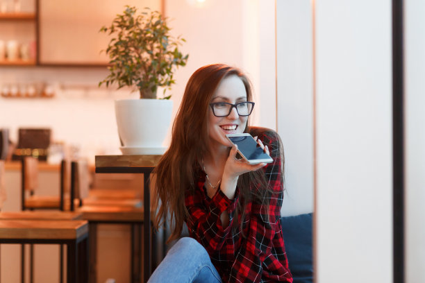 肖像迷人的年轻积极的女人在休闲衣服谈论智能手机坐在长凳上现代室内图片下载