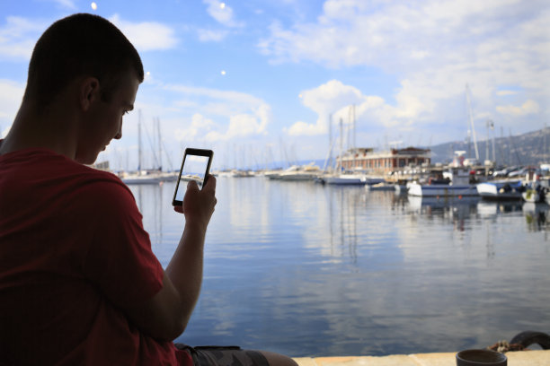 年轻的游客，用触摸屏，用智能手机拍照，照片短信。欣赏航海船、码头的景色。意大利的里雅斯特，亚得里亚海。图片下载