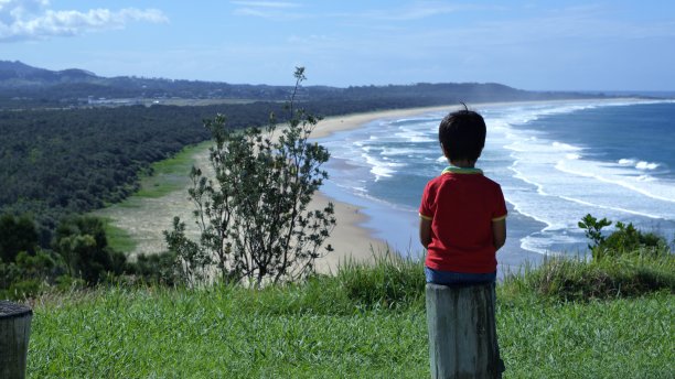 孩子坐在木桩上，看着大海、陆地的全景图片下载