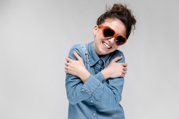 年轻的黑发女孩戴着心形的眼镜。头发梳成一个髻。那女孩双手紧抱着自己。图片下载