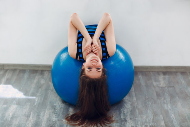 一个年轻女人坐在健身房的普拉提球上图片下载