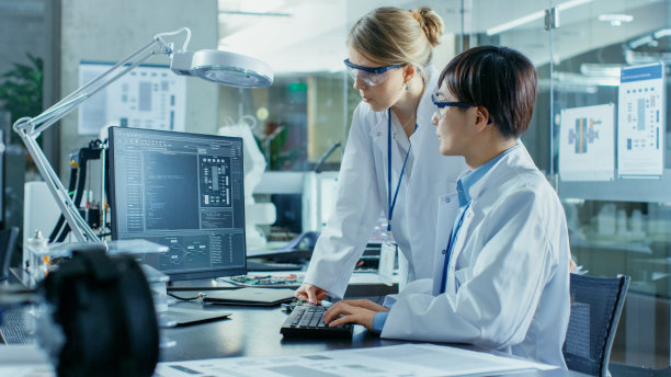 亚洲科学家坐在他的桌子上向年长工程师咨询复杂的编码和编程。在计算机科学研究实验室的机械臂模型。素材图片