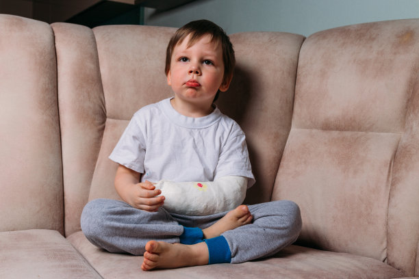 一个胳膊断了的小男孩坐在椅子上，打了石膏。医院。药。。疼痛。折断四肢。图片下载