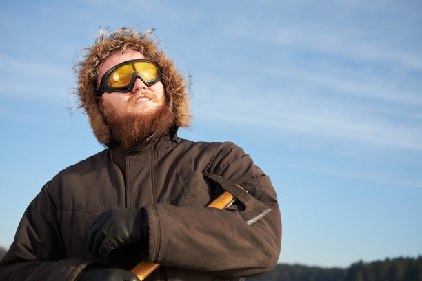年轻的蓄着胡须的男子，前额戴着滑雪板防护眼镜，用冰斧摆姿势图片下载