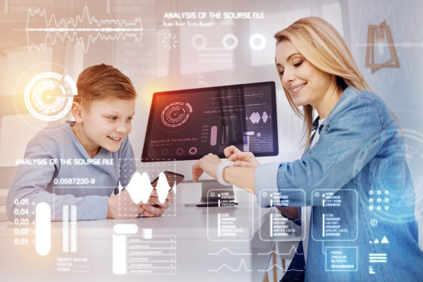 微笑的男孩拿着智能手机，而他的妈妈在看她的手表图片下载