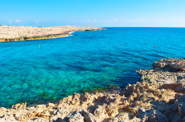塞浦路斯阿吉亚纳帕，Vathia Gonia海滩附近的海湾图片。粗糙的石灰岩海岸线，靠近深蓝色透明的蔚蓝海水，背景是岩石小山。秋天温暖的一天图片下载