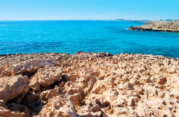 塞浦路斯阿吉亚纳帕，Vathia Gonia海滩附近的海湾图片。粗糙的石灰岩海岸线靠近深蓝色的海水和岩石小山的背景。秋天温暖的一天图片下载