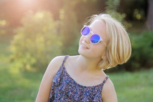 漂亮的金发小女孩戴着蓝色的太阳镜，阳光明媚温暖的夏日图片下载