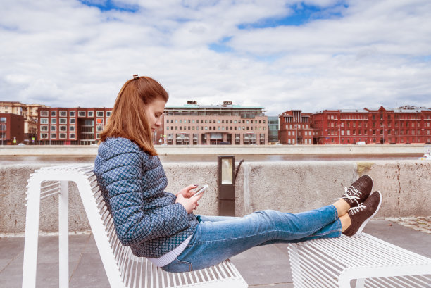 迷人的女孩放松地坐在码头上看你手机上的新闻图片下载