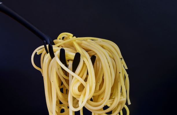 意面勺上的煮熟的意大利面。黑色背景上的意大利面特写。深色食物照片。文案空间图片下载