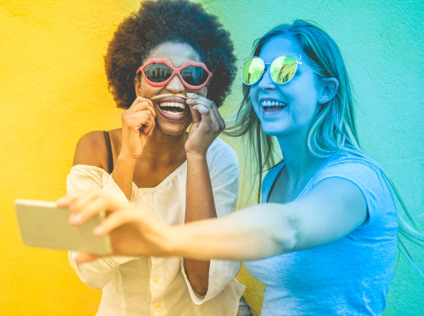 快乐的女性朋友在户外自拍-时髦的女孩戴着太阳镜一起欢笑-青春和友谊的概念-聚焦非洲女性的脸-蓝色和黄色的辐射滤镜图片下载