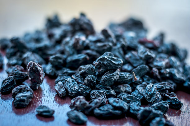 黑色葡萄干或kali kishmish或Zante醋栗放在白色的盘子里，在深色的哥特式表面上，以减少脱水的机会。图片下载