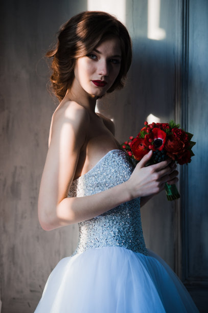 阳光躺在精致的新娘的脸上，而她站在窗口的白色连衣裙图片下载