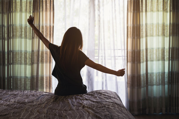 年轻的亚洲女人坐在床上，伸展自己在早上图片下载