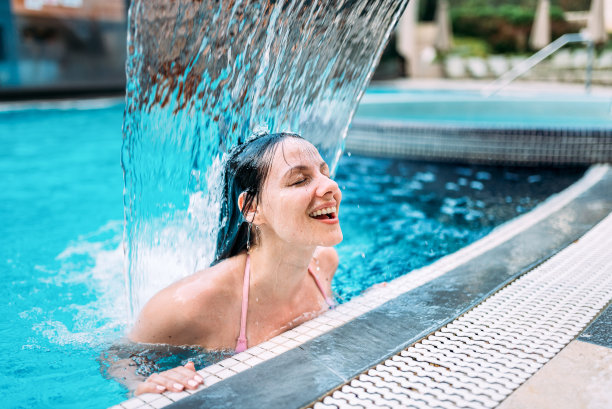 特写的年轻女子站在一个游泳池的瀑布下。图片下载