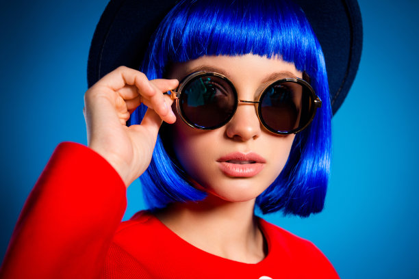近裁剪的肖像时尚优雅的女孩在夏季眼镜拿着眼与手看孤立在蓝色背景上的相机。休息放松休闲周末理念图片下载