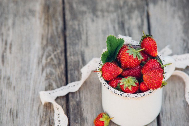 新鲜多汁的带叶草莓。质朴的搪瓷马克杯和手工花边。复古的杂志图片。图片下载
