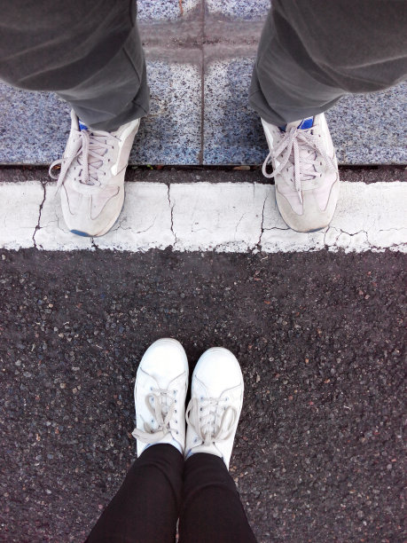 双脚踩在沥青上。人行道上有两双鞋。图片下载