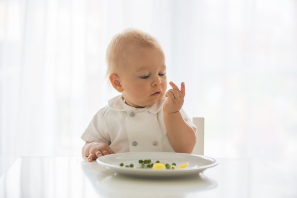 蹒跚学步的孩子，穿着白衬衫的可爱男孩，在家吃豌豆图片下载