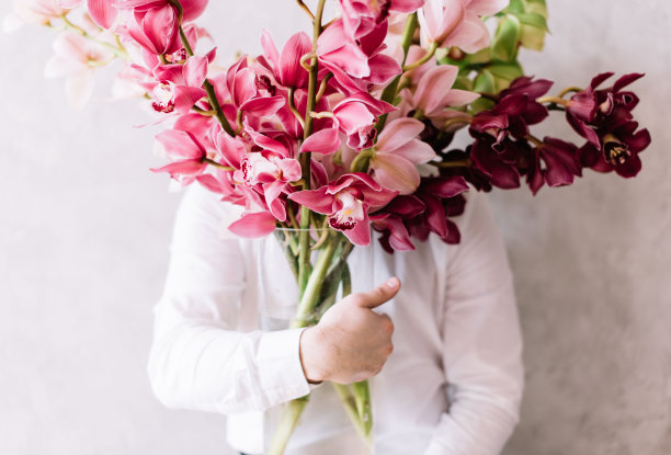 一个很不错的年轻人，穿着一件白衬衫，手里拿着一大束兰花，遮住了他的脸图片下载