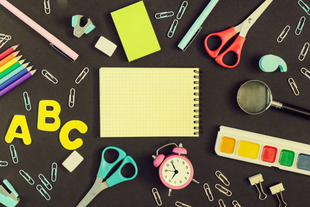 照片从上面，在中间的黑色是一个笔记本与文字或题词的地方，模拟。附近有丰富多彩的学校和办公用品。图片下载