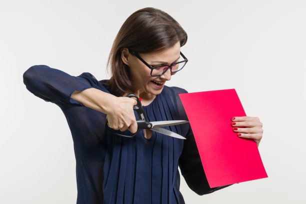 一个女人拿着剪刀和一张纸，剪着纸。图片下载