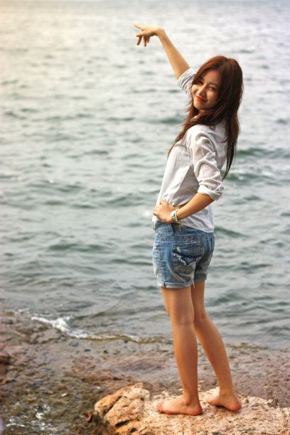 微笑的亚洲年轻女子指着，看着站在岩石上的相机图片下载