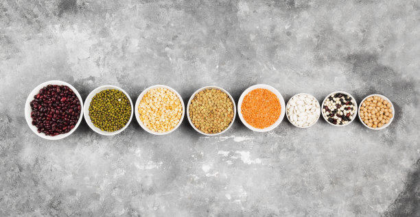 各种各样的豆子(红扁豆，绿扁豆，鹰嘴豆，豌豆，红豆，白豆，混合豆，绿豆)在灰色的背景。前视图。食品的背景素材图片