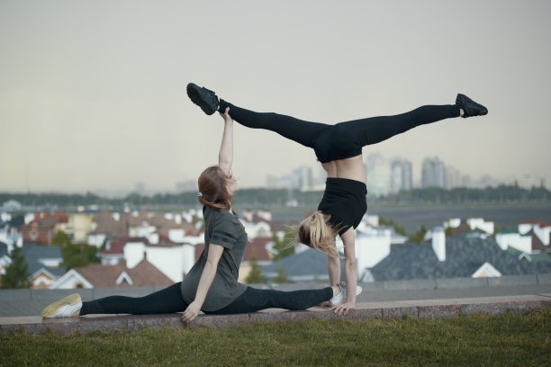 两个年轻的女体操运动员做杂技元素与城市景观的背景图片下载