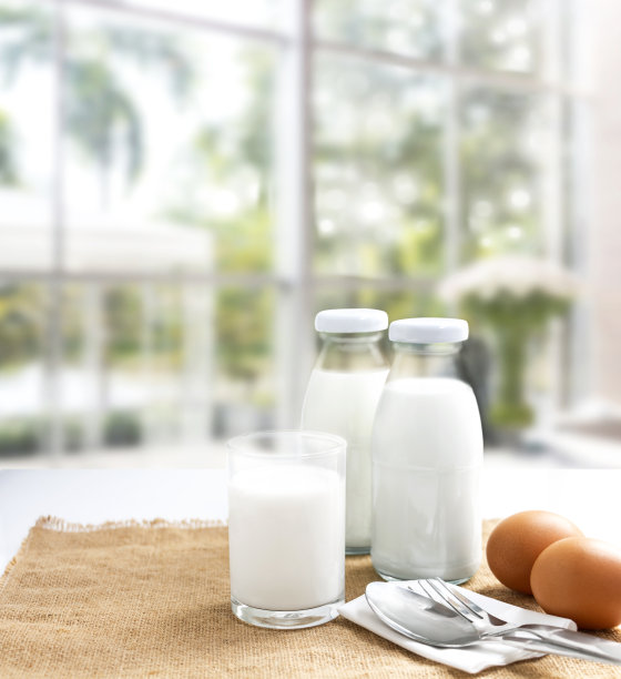 两个玻璃瓶和一杯牛奶。用叉子和勺子放在麻布袋上的鸡蛋在商店的背景。与复制空间的文本。图片下载