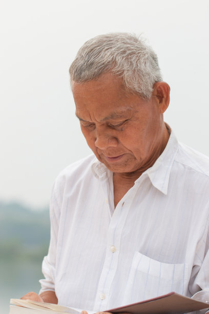 成人教育学习理念:快乐亚洲老人坐在河边户外看书学习或自我放松图片下载