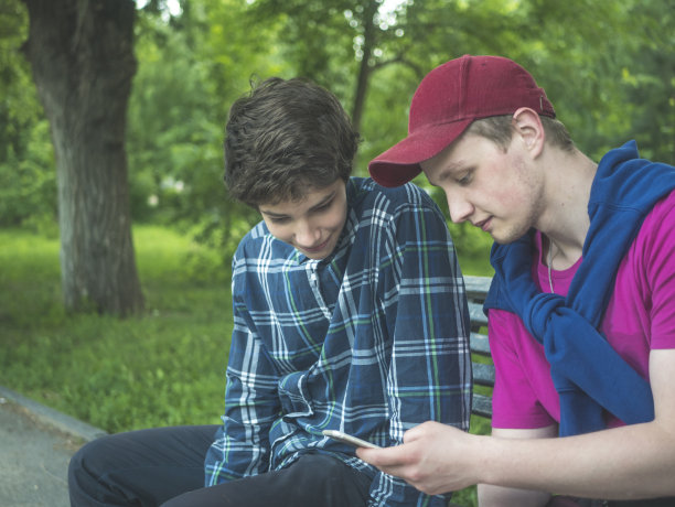 一个夏日的公园里，两个年轻的帅哥在社交网络上查看动态图片下载