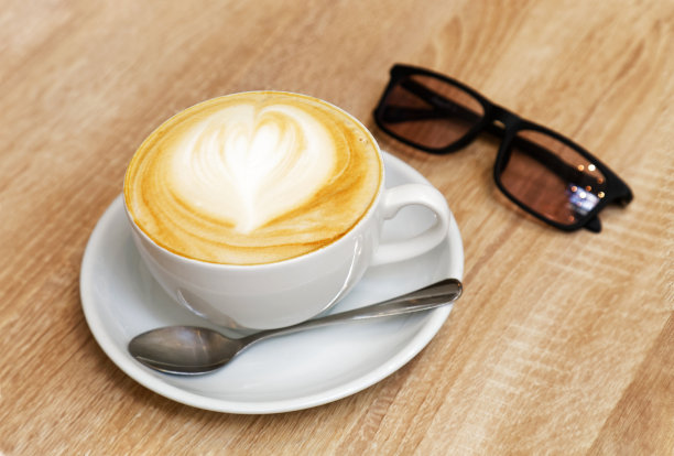 木桌上放着白色的卡布奇诺咖啡和太阳镜图片下载