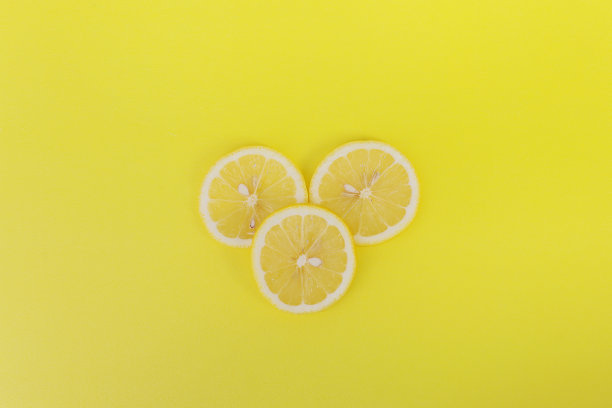 三片新鲜的柠檬片在黄色的背景上。图片下载