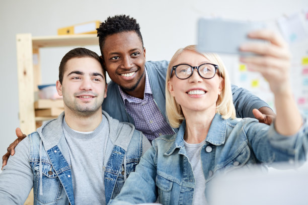 乐观的多民族办公室同事们穿着休闲服装在智能手机上自拍在社交媒体上工作图片下载