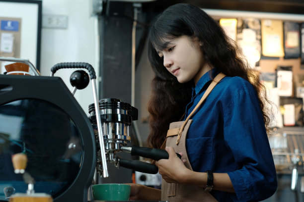 年轻的亚洲女性咖啡师在柜台咖啡馆制作咖啡背景，人们在食品和饮料行业，小企业和现代工作场所的概念图片下载
