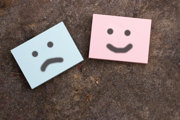 悲伤和快乐的笑脸画在贴纸上，深灰色纹理的背景。情感的概念图片下载