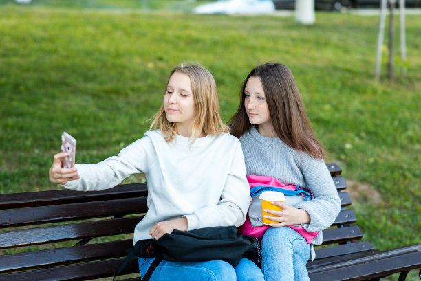 两个女孩女生。在夏天的公园里，在街上的青少年。可以端一杯咖啡或茶。用手机拍照。学校朋友的概念。大自然的照片。图片下载